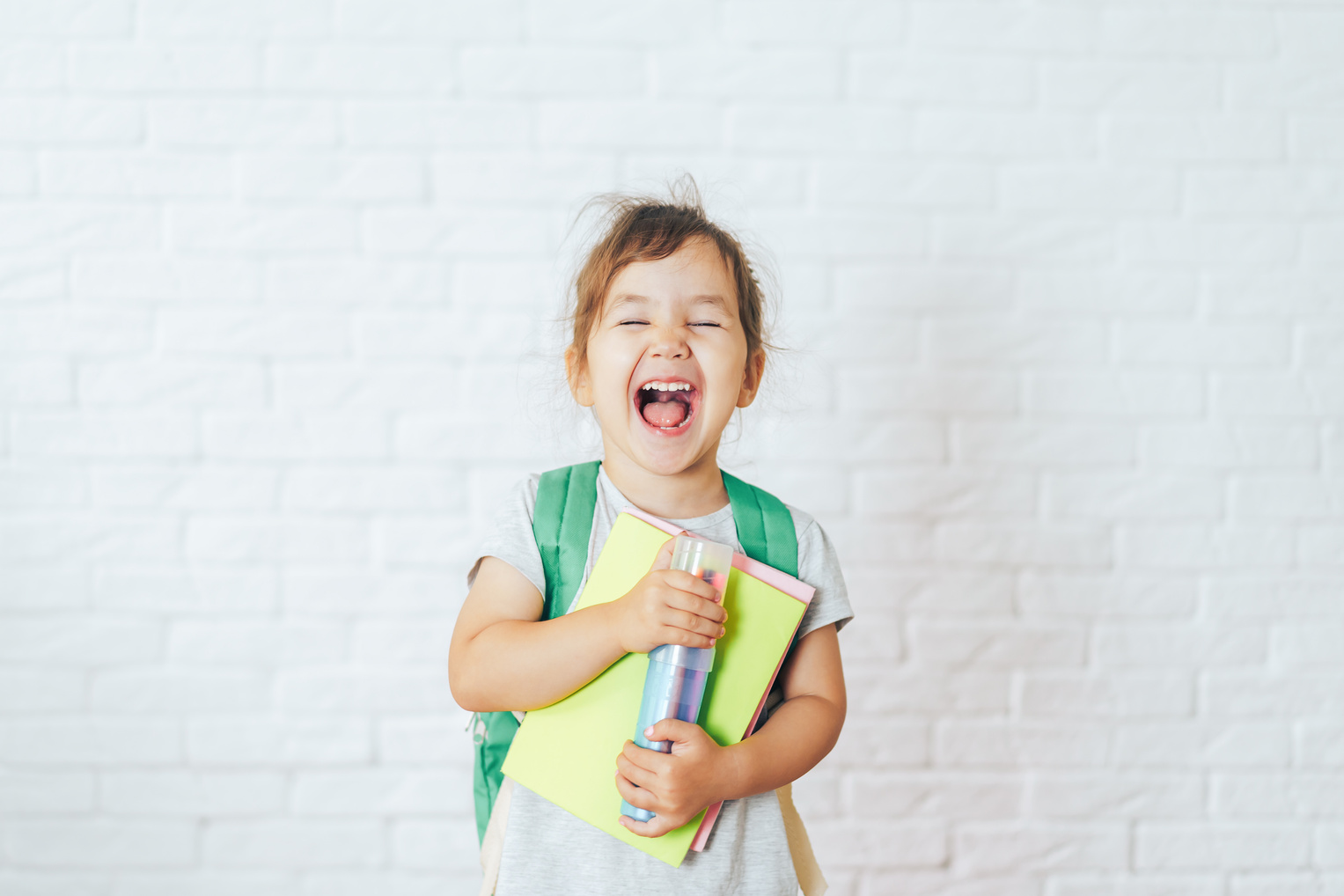Child with green backpack holding school supplies